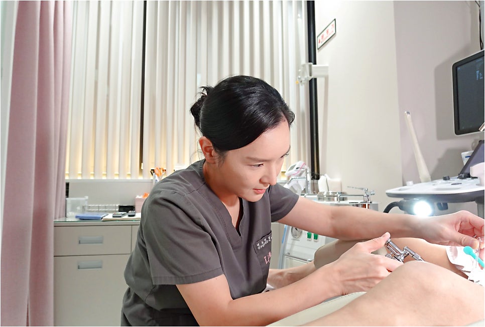회색 스크럽 착용 의료진이 진료대의 환자 다리 부위에 기기로 시술 중