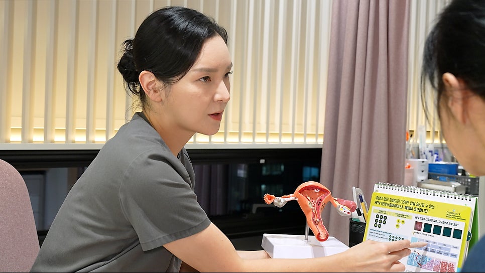 회색 스크럽 의료진이 자궁 모형을 들고 있으며, 펼쳐진 책자에 HPV(인유두종바이러스) 백신 관련 문구와 G