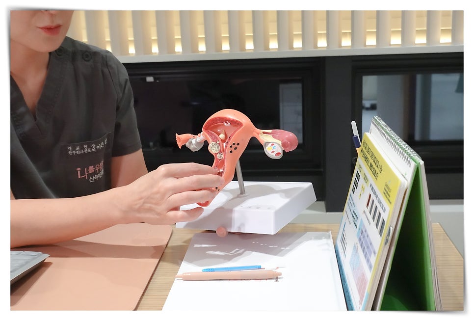 벽면 모니터 옆에서 흰 가운 소매를 입은 손이 흰색 원통형 프로브를 들고 있고, 모니터에는 수치와 목록이 담