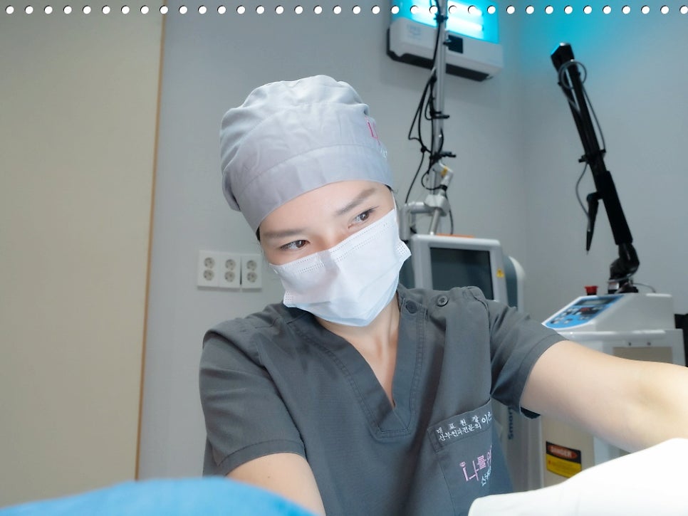 수술모와 마스크를 쓴 의료진이 레이저 장비 옆에서 팔을 뻗고 있다