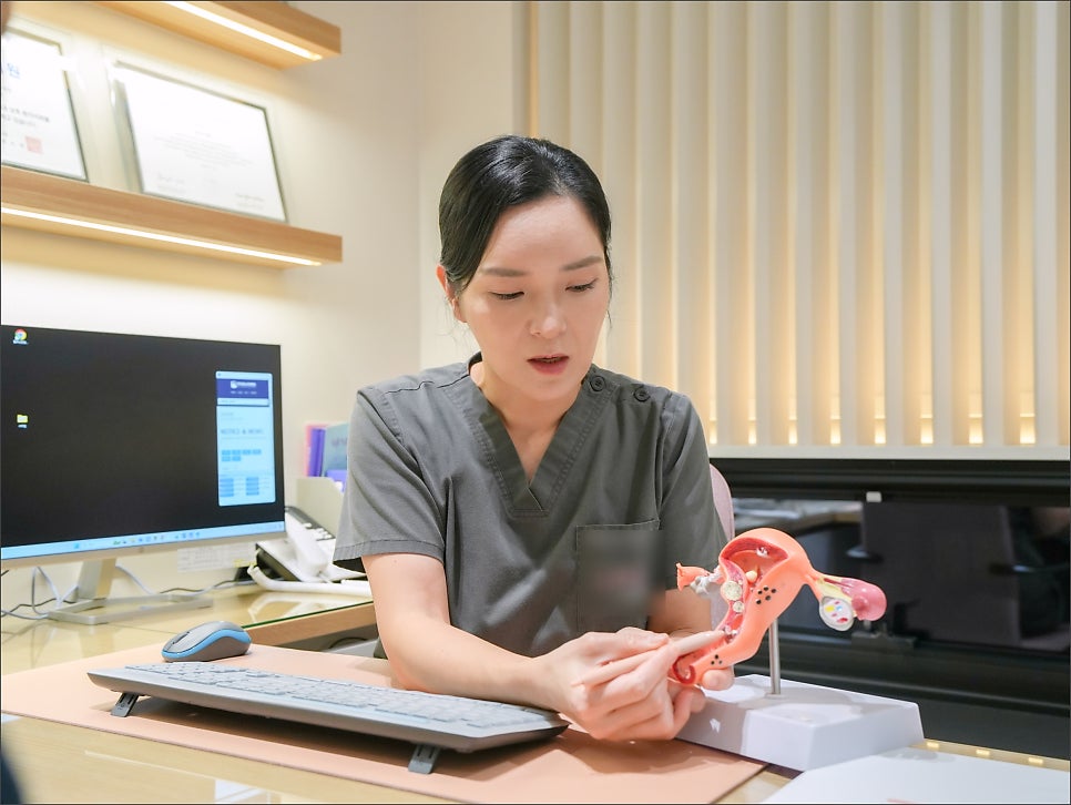 회색 유니폼을 입은 여성 스태프가 펜으로 자궁 모형을 가리키며 설명하는 모습