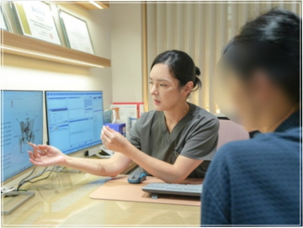 여성 직원이 두 대의 모니터(왼쪽에 골반 해부도) 앞에서 팔을 뻗어 설명하는 모습
