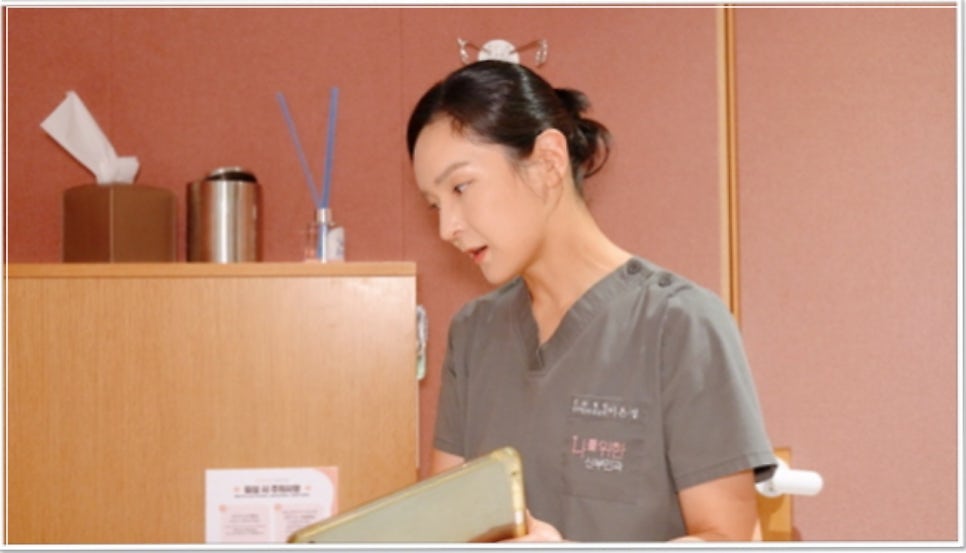 회색 스크럽을 입은 의료진이 태블릿을 든 채 안내 데스크에서 이야기하는 모습