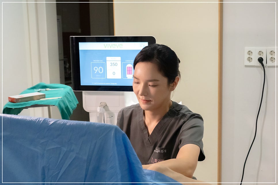 회색 스크럽을 입은 여성 의료진이 파란 수술포가 덮인 환자 옆에서 몸을 숙이고 있고, 뒤편 모니터에 vive
