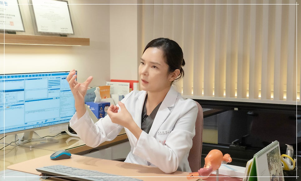 흰 가운을 입은 의료진이 손을 들어 제스처하며 설명하는 진료실 장면